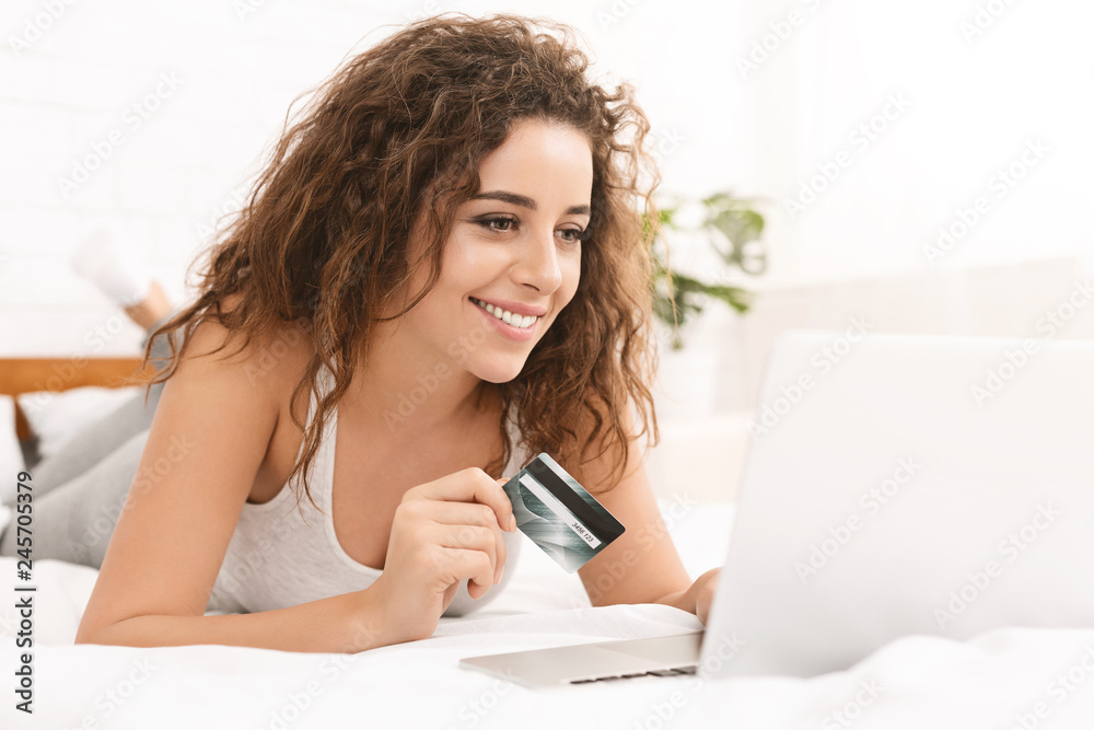 Woman using her credit card and laptop in bed