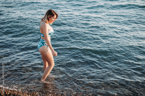 Beautiful young woman goes to the beach in bikini with beautiful body on tropical beach. Female fashion model posing in swimsuit on sea shore