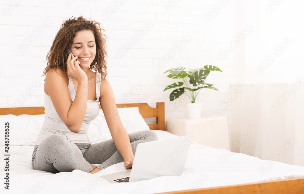 Young woman working on laptop and talking on phone in bed Young woman working on laptop and talking on phone in bed