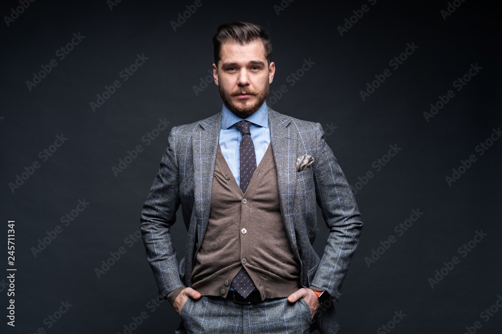 Fototapeta premium A confident elegant handsome young man standing in front of a black background in a studio wearing a nice suit.