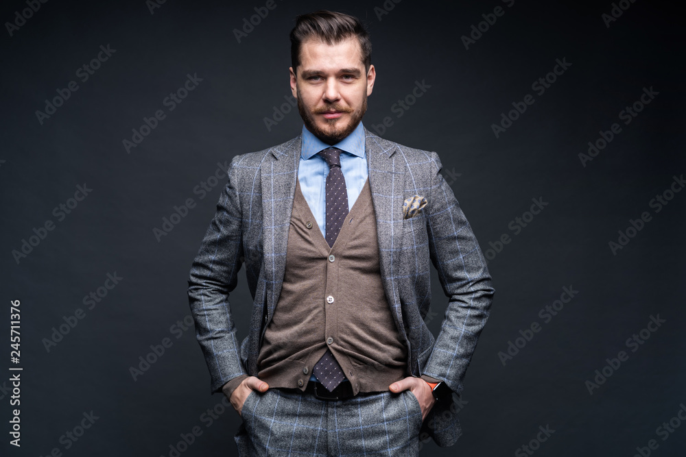 Fototapeta premium A confident elegant handsome young man standing in front of a black background in a studio wearing a nice suit.