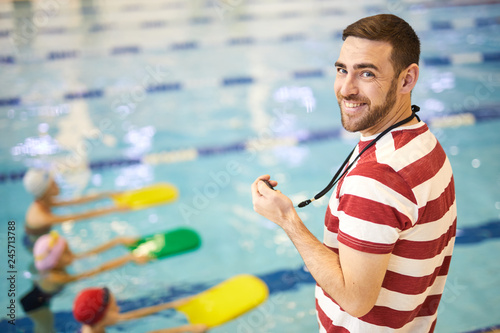 Portrait of smiling young swimming instructor training his group in the swimming pool