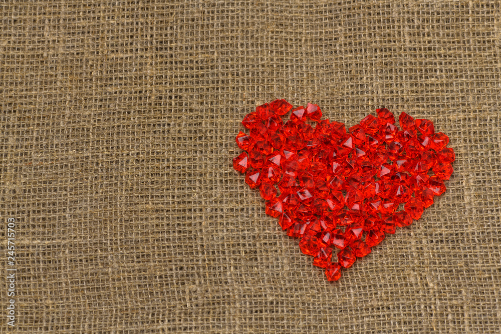 .Valentine's day. A large red plastic glass heart of small crystals lies on a brown burlap (bag). Horizontal photography.