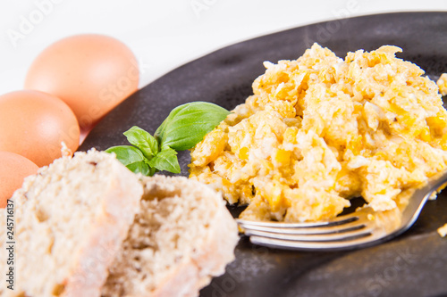 Scrambled eggs, some fresh eggs and wholemeal bread, and a fork, decorated with basil, on a white background 