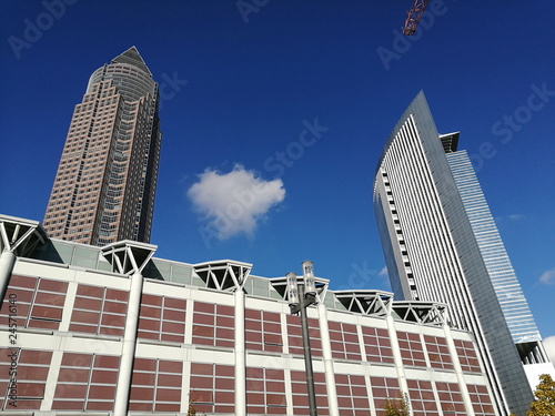 Fassade einer modernen Messehalle miit hohem Büroturm im Hintergrund vor blauem Himmel mit weißer Wolke im Sonnenschein am Europaviertel in Frankfurt am Main in Hessen photo