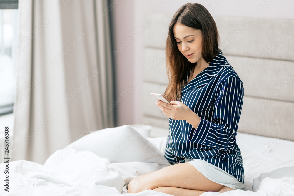 nice pleasant young woman is sending messages, browsing the Net, surfing the Internet, reading e-book, looking at the screen while resting in the bedroom. close up photo nice pleasant young woman is sending messages, browsing the Net, surfing the Internet, reading e-book, looking at the screen while resting in the bedroom. close up photo