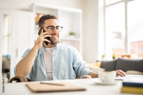 Tableau sur toile Happy young businessman with smartphone consulting with colleague while sitting