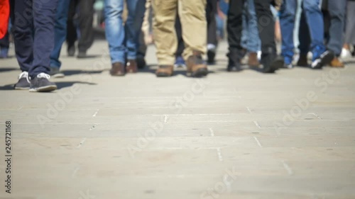 Slow motion feet walking forward. Low angle, slow motion video footage with shallow focus on the foreground pavement as an anonymous crowd walks into frame.
