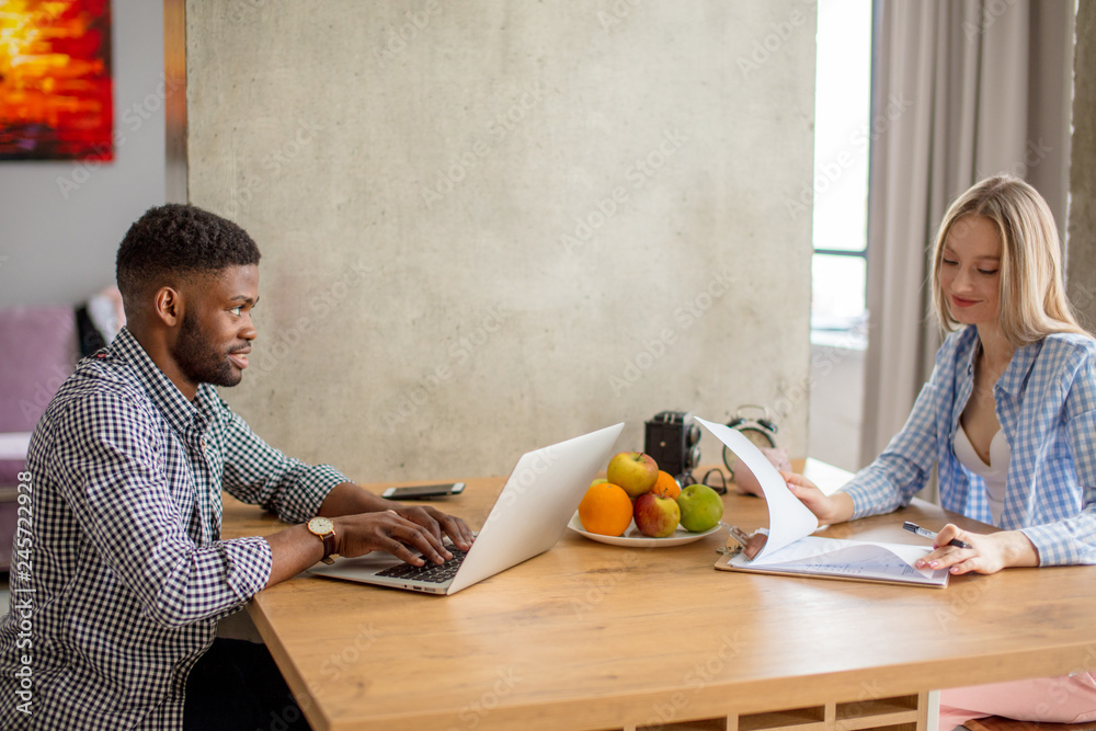 Young multi-ethnic couple sit opposite each other at the kitchen floor, planning their future vacations, make calculations, develop a route. People, vacation, planning concept