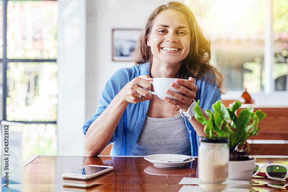 Beautiful young happy girl student sitting in a cafe at the table with a cup of tea in her hands Beautiful young happy girl student sitting in a cafe at the table with a cup of tea in her hands