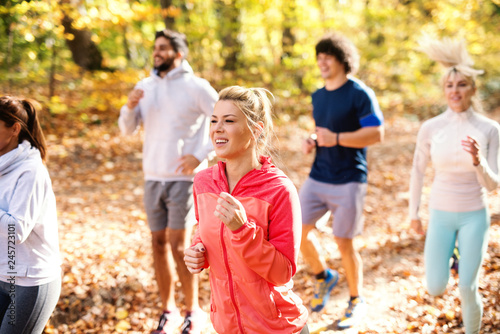 Small group of people running in woods in the autumn. Selective focus on blonde woman.