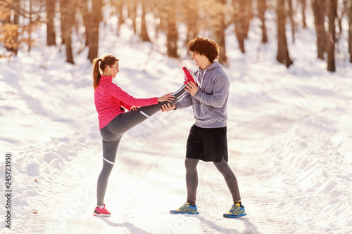 Man helping woman to stretch leg before running. Wintertime, healthy lifestyle concept.