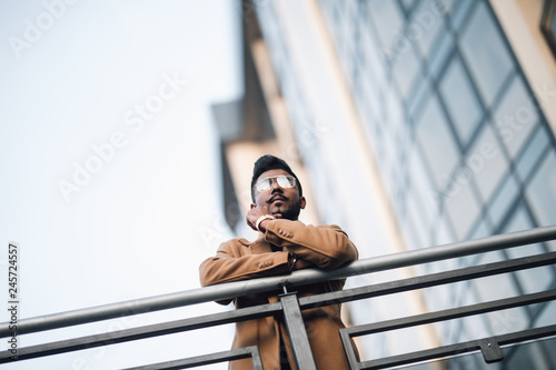 Young happy Indian businessman smiling with arms on handsrail at rooftop of business center photo
