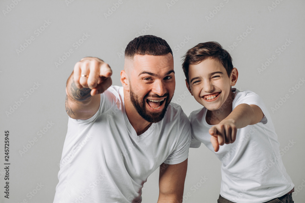 laughing daddy and son pointing at the camera. close up shot. happiness, positive emotion. isolated grey background. fun laughing daddy and son pointing at the camera. close up shot. happiness, positive emotion. isolated grey background. fun