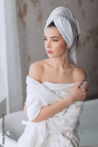 Portrait of a beautiful seductive young brunette lady with bare shoulders, let her bathrobe bare tender frigile body in bathroom.