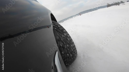 Pov shot car wheel speed moving surrounded by white snow near forest park. High angle black automobile fast move on countryside road race competition at cold winter day