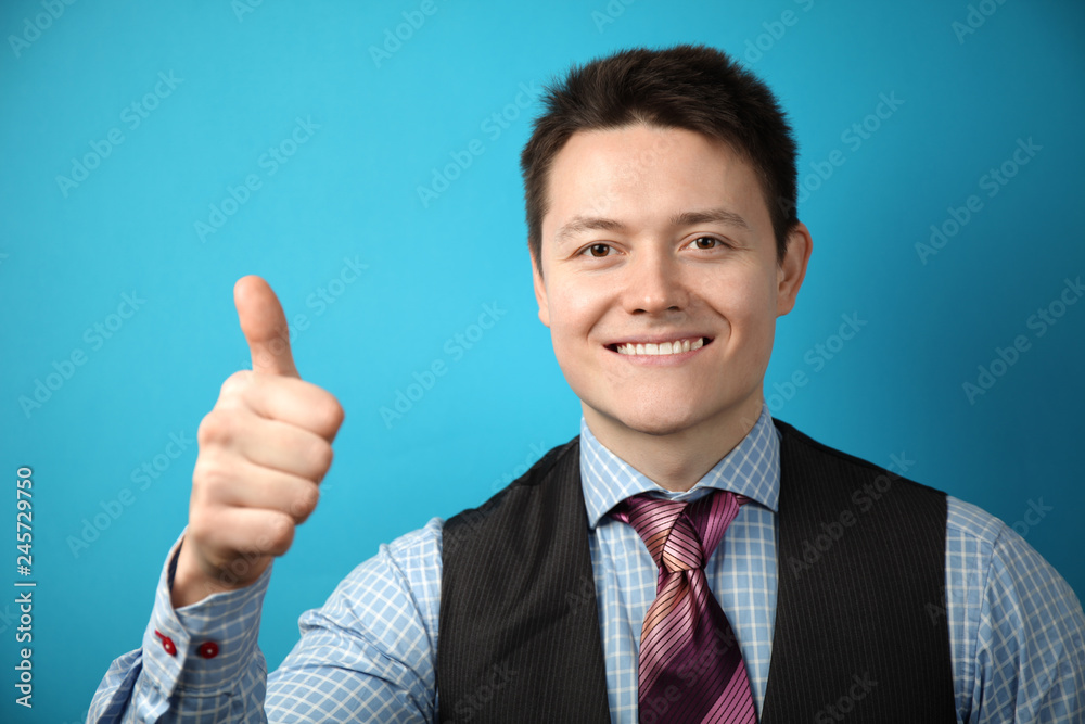 Young businessman in suit on blue background shows his hand thumbs up, symbol of success. Young businessman in suit on blue background shows his hand thumbs up, symbol of success.