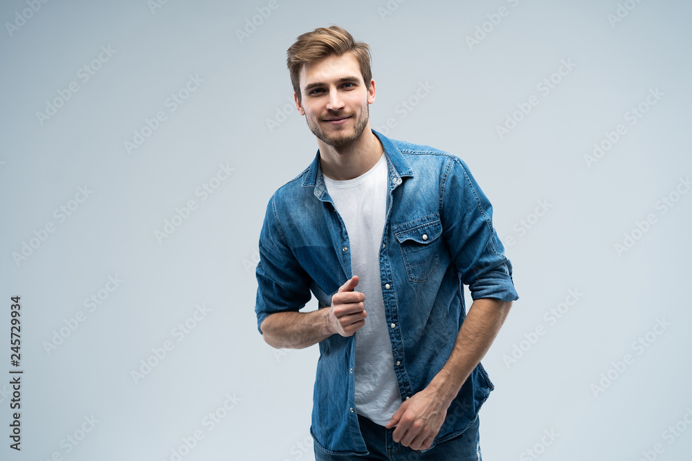 Portrait of stylish, stunning man in denim outfit standing over grey ...
