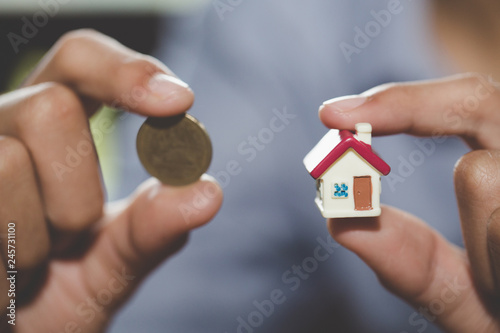 Investor show hand holding a model home and coin , Saving money for buy a new house and loan for plan business investment for real estate in the future concept.