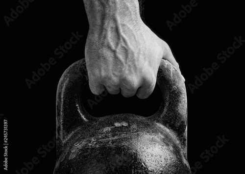Kettlebell on a black background. The fist of an athlete clutching kettlebell. Close-up of a muscular hand holding a kettlebell photo