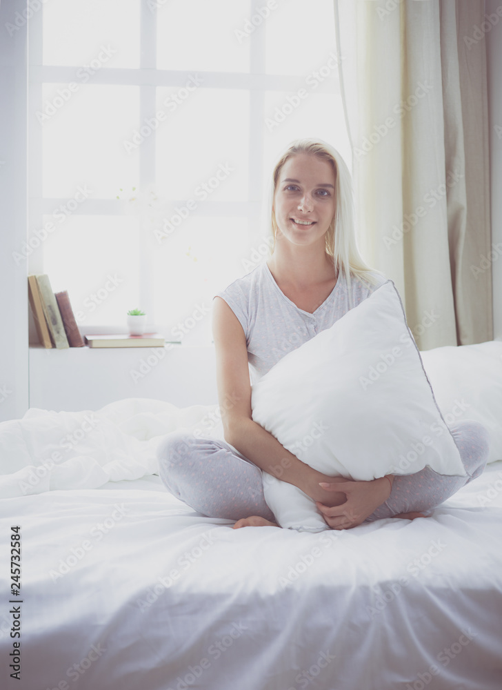 Cute woman holding a pillow while sitting on her bed Cute woman holding a pillow while sitting on her bed