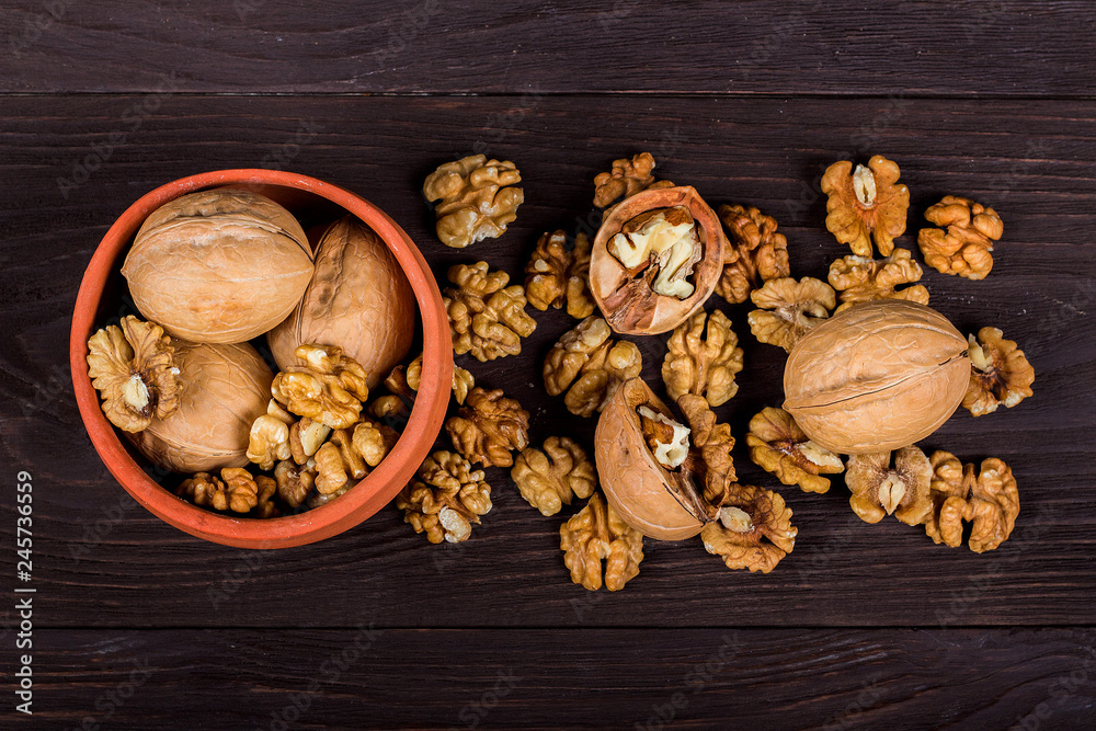 Fototapeta premium whole walnuts and kernels on wooden background, walnut on a dark old table in a clay pot