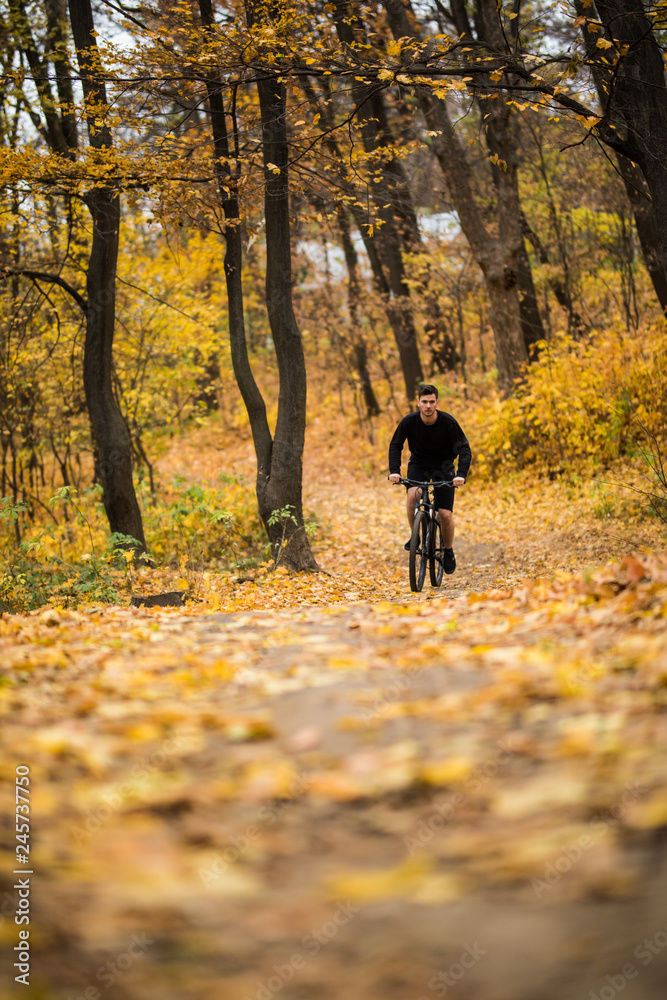Young athlete ride with bicycle on the autumn park. Preparing for training Young athlete ride with bicycle on the autumn park. Preparing for training