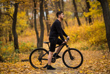 Handsome man biker in professional sportswear looking to side while riding bike down park alley on autumn day. Sportsman training thinking about future win in contest. 
