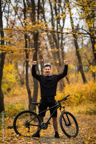 Fototapeta Naklejka Na Ścianę i Meble -  Young handsome man biker after training with raised hands in autumn forest track