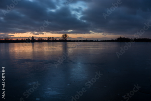 Cloudy sky after sunset from the frozen lake and reflecting light on the ice © darekb22