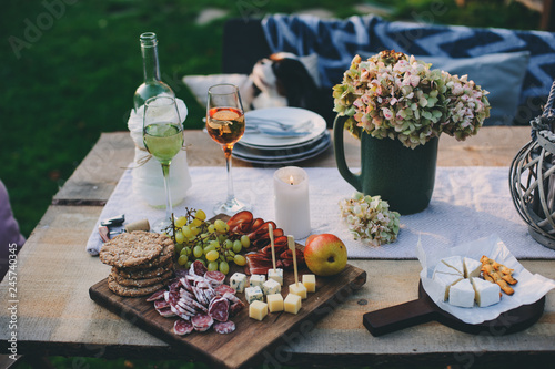 wine, cheese, ham and fruits served on wooden cutting board. Summer outdoor garden party