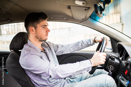 Young man sits in a newly bought car holding his hands on a rudder