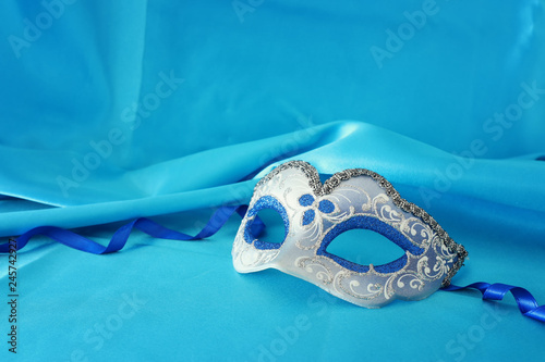 Photo of elegant and delicate silver and blue venetian mask over turquoise silk background.
