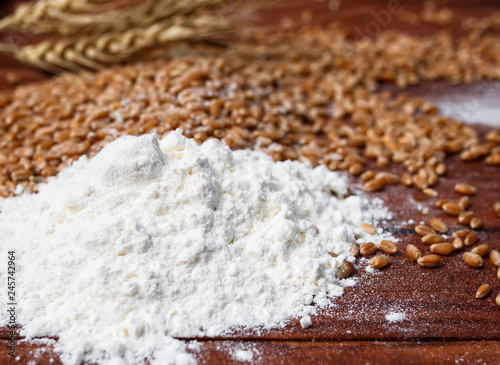 background of Golden wheat grains and white crumbling flour scattered on wood...