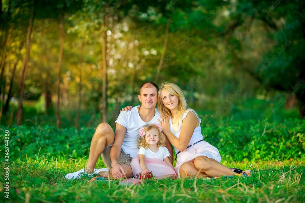 Happy family in a beautiful spring park, sitting on the grass hugging and smiling, healthy outdoor recreation Happy family in a beautiful spring park, sitting on the grass hugging and smiling, healthy outdoor recreation