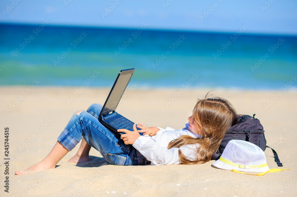 work in travel, girl teenager lies on the beach with a laptop