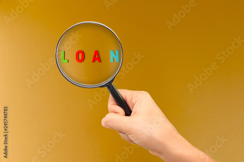 Woman hand hold a magnifying glass searching for a text with loan on brown background, Loan money investment to the future concept.