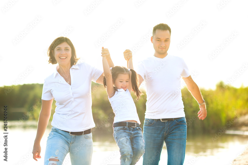 A happy family walks along the river bank on a sunny day, will barefoot on the water and splash, healthy outdoor recreation