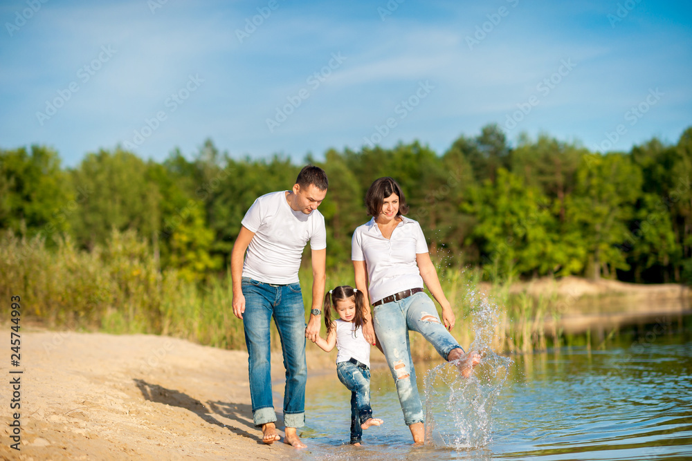A happy family walks along the riverbank on a sunny day, will barefoot on the water and splash A happy family walks along the riverbank on a sunny day, will barefoot on the water and splash