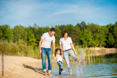 A happy family walks along the riverbank on a sunny day, will barefoot on the water and splash