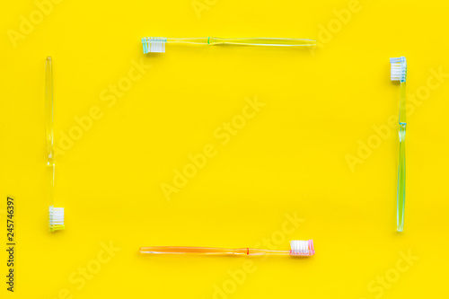 Clean teeth. Plastic toothbrushes on yellow background top view copy space frame