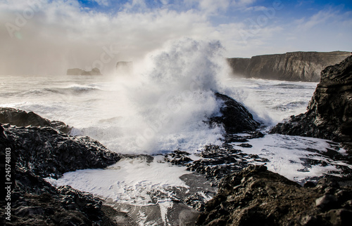 a huge wave from the Atlantic Ocean covers black volcanic stone on the black lava sand bank in Iceland