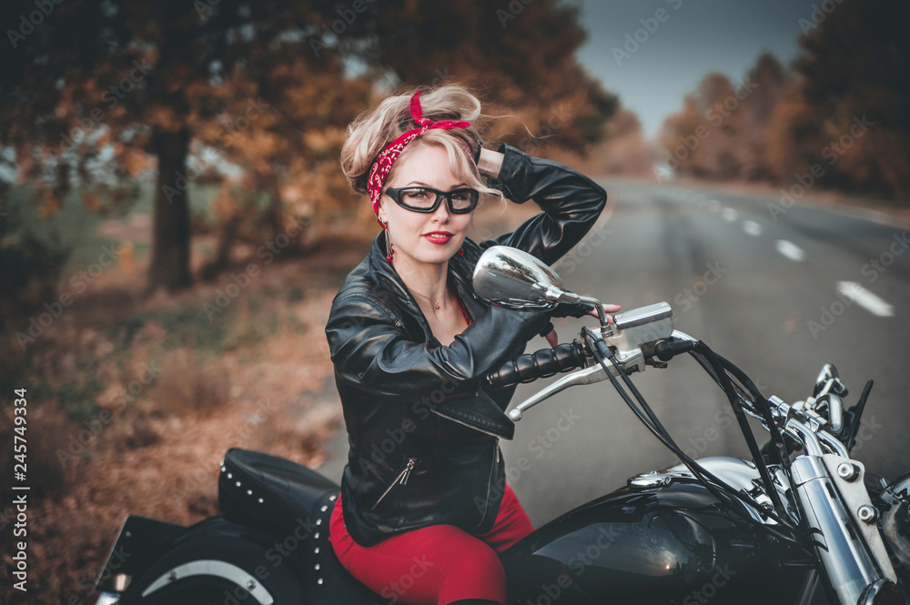 Beautiful biker woman posing outdoor with motorcycle. Pin-up style.
