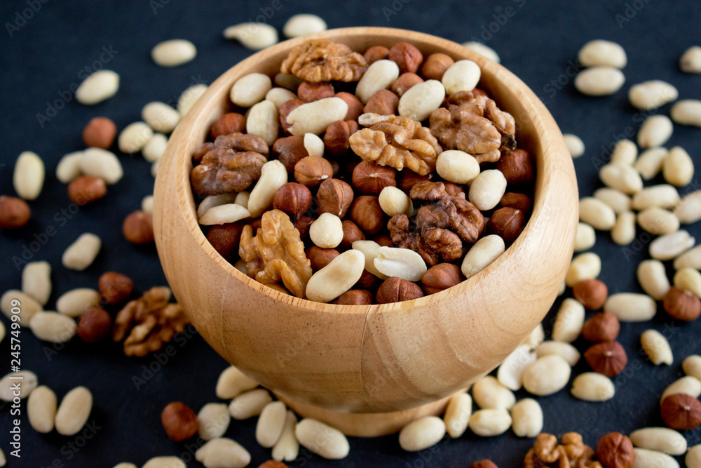 hazelnuts, peanuts, walnuts in wooden bowl on black background