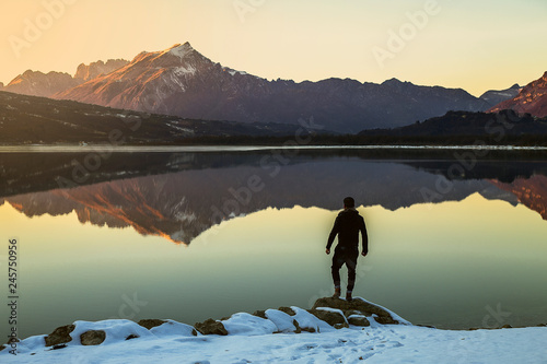 Man reaches rock above lake, arms outstretched.