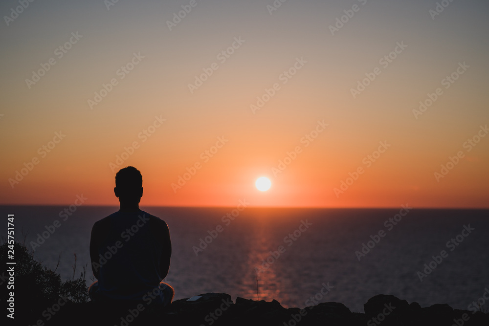 Young man looking to the sunset over sea. Enjoying and relaxing concept, full of unforgettable experiences to recharge. Balance mind and body