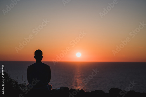 Young man looking to the sunset over sea. Enjoying and relaxing concept, full of unforgettable experiences to recharge. Balance mind and body