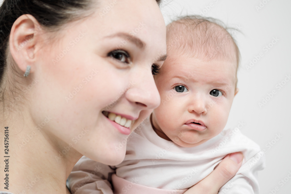 Young woman mother in denim overalls holds a baby child in her arms. White background in the studio. Young woman mother in denim overalls holds a baby child in her arms. White background in the studio.