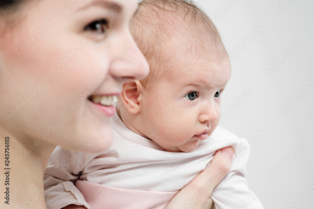 Young woman mother in denim overalls holds a baby child in her arms. White background in the studio.