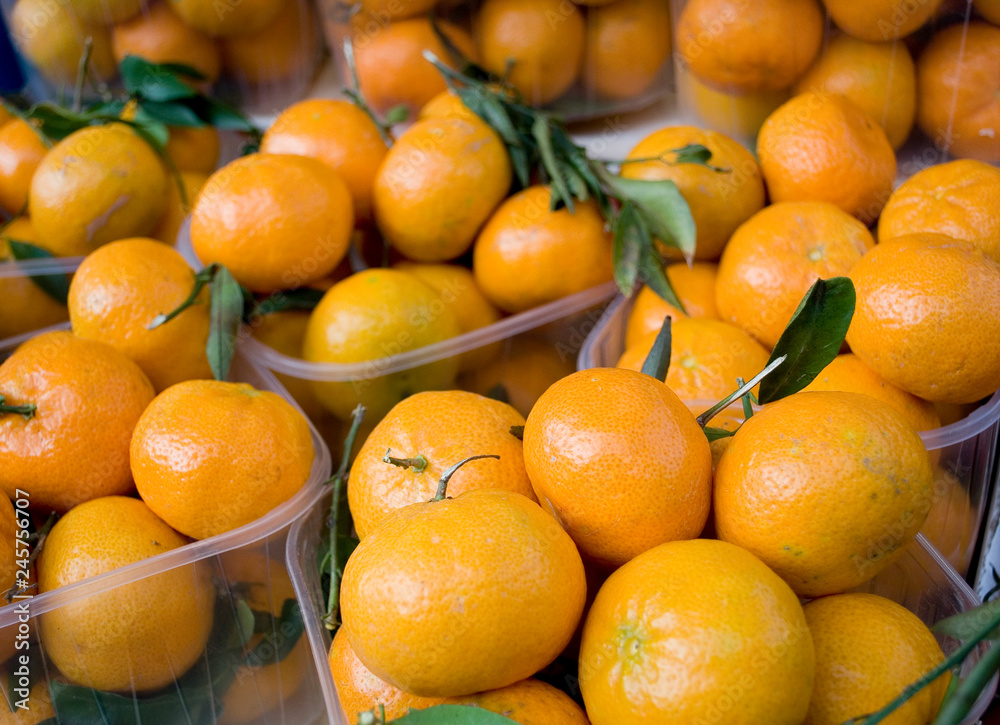 Tangerines (mandarins, clementines, citrus fruits) with green leaves, in a plastic basket, at local fruit market, orange, agriculture, food, diet, vitamins, nourishment, nutrition, Milan, Italy Tangerines (mandarins, clementines, citrus fruits) with green leaves, in a plastic basket, at local fruit market, orange, agriculture, food, diet, vitamins, nourishment, nutrition, Milan, Italy
